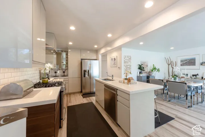 Kitchen featuring an island with a sink, stainless steel appliances, white subway tile backsplash, recessed lighting, and wood-finish flooring