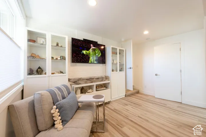 Wood-finish flooring, recessed lighting, built-in display cabinetry, and a white brick-finish accent wall
