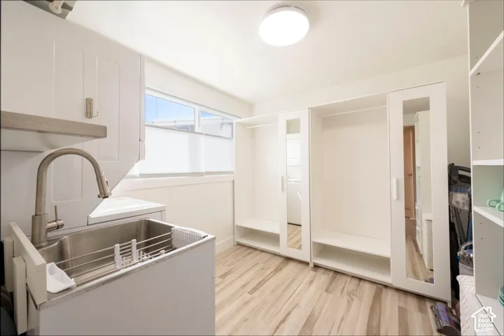 Integrated utility sink with a brushed nickel faucet, wood-finish flooring, built-in white cabinetry, mirrored closet doors, and a flush-mount ceiling light