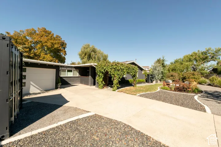 Mature landscaping with varied foliage, concrete driveway, attached garage, and exterior brick accents