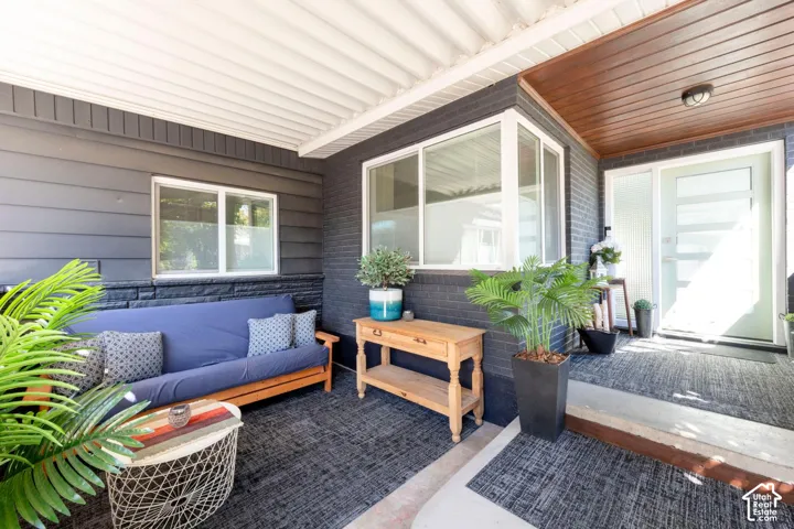 Covered porch featuring a light gray entry door, large windows, dark brick, and horizontal siding