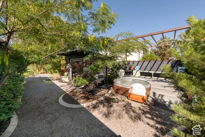 Gravel pathway bordered by mature trees and shrubs, leading to a raised deck with a wooden pergola