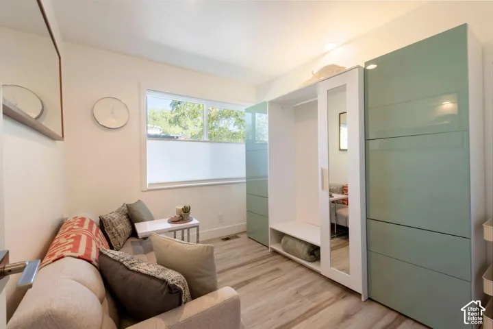 Wood-finish flooring, built-in storage with mirrored panels, window with cellular blinds, recessed lighting, and a neutral wall color