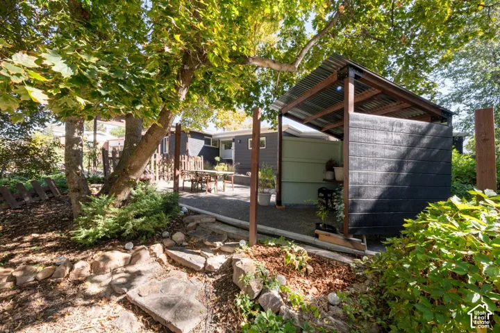 Gravel patio area, dedicated covered outdoor structure, mature trees, and natural landscaping with stone accents