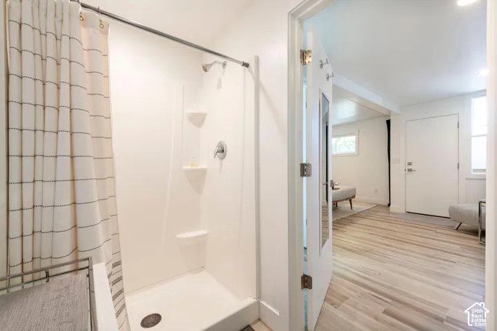 Shower with integrated shelving, chrome fixtures, and wood-finish flooring