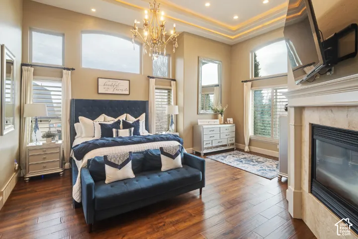 Luxurious primary suite showcasing a wood-finish plank floor, crown molding with recessed ceiling detail, and a crystal chandelier