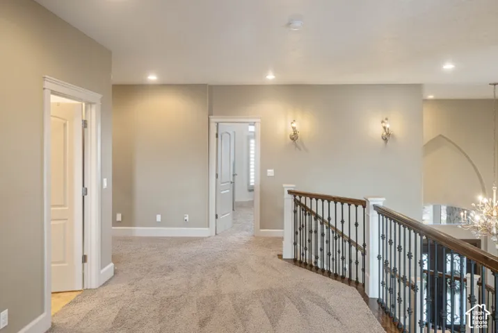 Carpeted hallway featuring recessed lighting, decorative wall sconces, white paneled doors, and a wood and wrought iron staircase railing