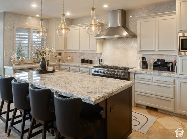 Center island with a stone countertop, custom cabinetry, stainless steel range with matching hood, and mosaic tile backsplash