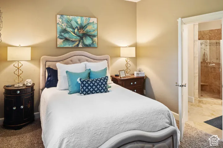Bed frame with upholstered headboard, carpet flooring, and an adjoining bathroom with a glass-enclosed shower