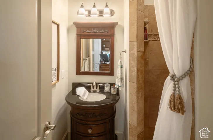 Vanity with dark countertop, carved wood-finish cabinetry, and framed mirror with integrated lighting