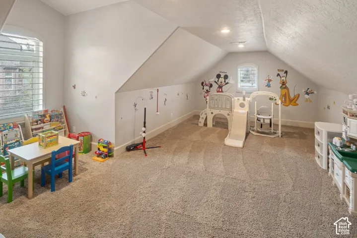 Carpeted room with a vaulted ceiling, multiple windows, and recessed lighting