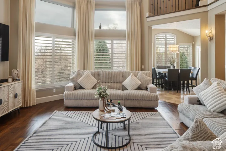 Two-story living area with dark wood-finish flooring, tall windows with plantation shutters, and an open-concept design
