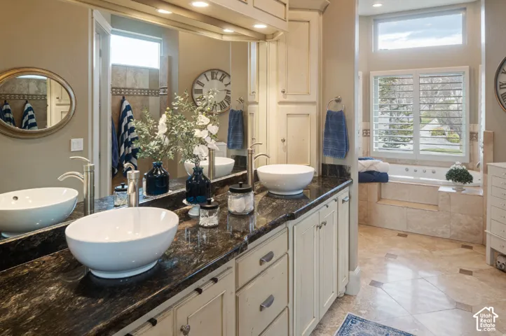 Spa-inspired primary bathroom featuring dual vessel sinks with polished stone countertops, custom white cabinetry with brushed nickel hardware, and abundant natural light from multiple windows