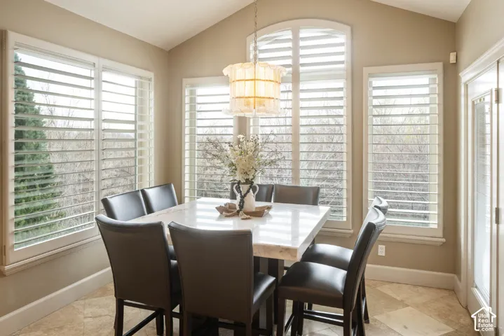 Vaulted ceiling, multiple windows with plantation shutters, arched window detail, tile flooring, and a glass-paneled door