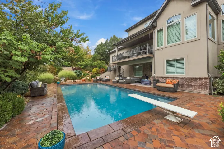 Rectangular swimming pool with a diving board, extensive brick paver decking, multi-level landscaping, and a covered patio with a spiral staircase