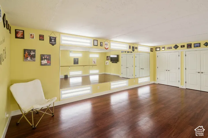 Wood-finish flooring with a mirrored wall, built-in barre, and multiple closet doors