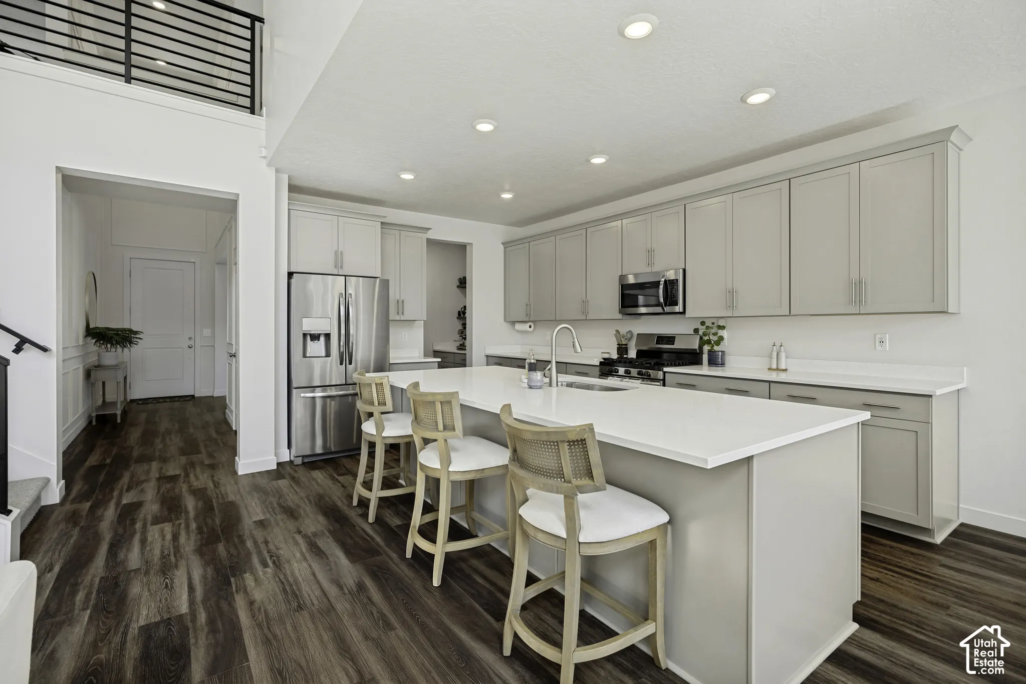 Kitchen featuring a large island with white countertops, light gray cabinetry, stainless steel appliances, and dark wood-finish flooring