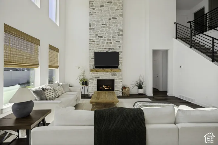 Two-story great room featuring a floor-to-ceiling stone-clad fireplace with a wood mantle, high ceilings, and a modern black metal staircase railing