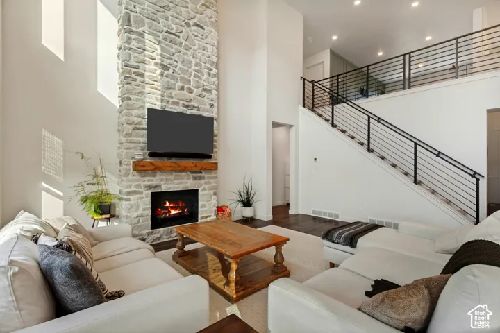 Two-story living area featuring a stone fireplace with wood mantel, high ceilings, dark wood-finish flooring, and a staircase with metal railings