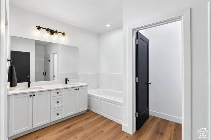 Wood-finish flooring, dual vanity with white cabinetry, quartz countertop, and matte black fixtures