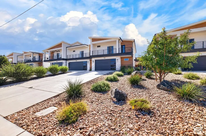Contemporary architectural style featuring clean lines, multiple balconies with black railings, wood-look accents, and stone veneer detailing