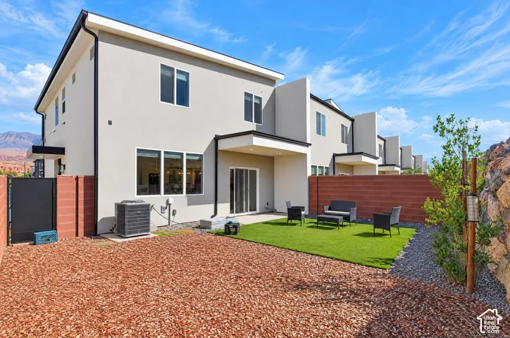 Contemporary stucco exterior with black trim, sliding glass door, multi-pane windows, artificial turf lawn, and a privacy wall