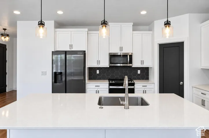 Kitchen featuring a large island with an undermount sink, white cabinetry, integrated stainless steel appliances, and a black hexagonal tile backsplash