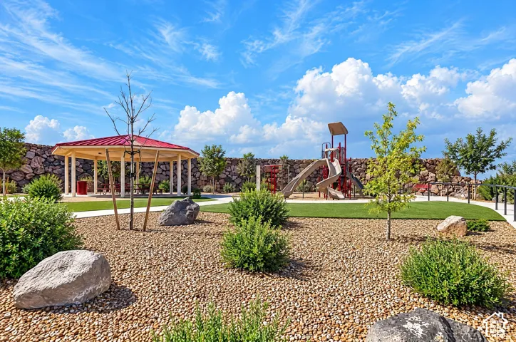 Community park featuring a gazebo with red roof, children's play structure, artificial turf, and a stone wall perimeter