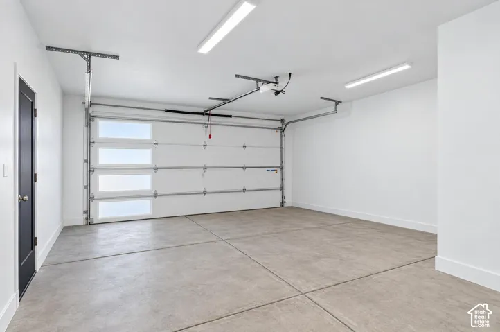 Spacious garage featuring a modern sectional overhead door with frosted windows, concrete flooring, crisp white walls, and bright overhead lighting