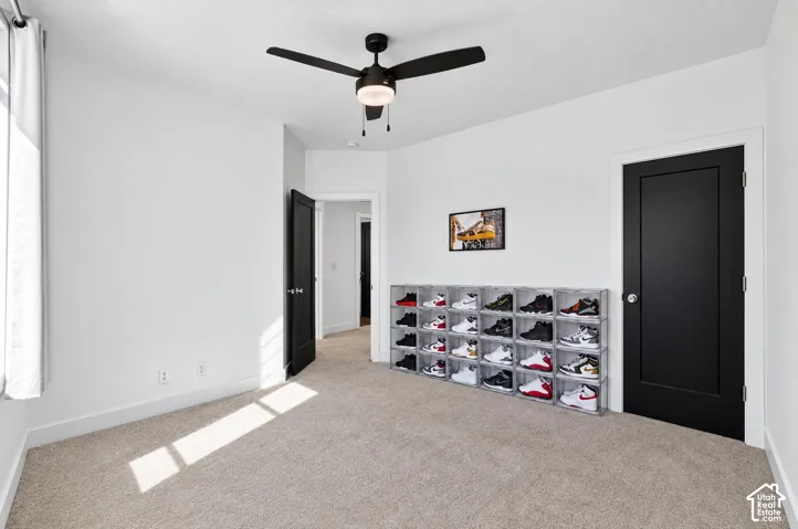 Neutral-toned carpeting, white walls, black interior door, and a black ceiling fan with integrated lighting