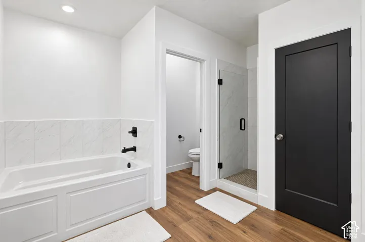 White paneled bathtub with matte black fixtures, white subway tile surround, and wood-finish flooring