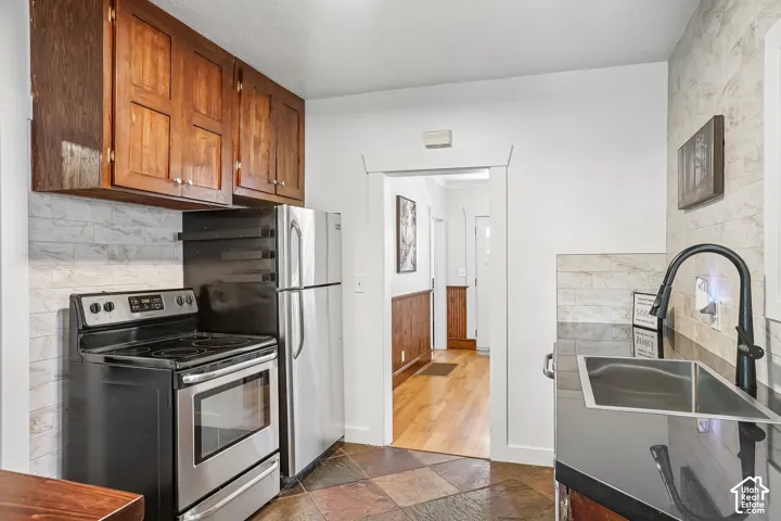 Dark wood-finish cabinetry, stainless steel appliances, patterned backsplash, a stainless steel sink, and a black faucet