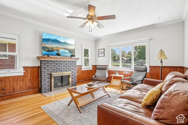 Hardwood flooring, brick-surround fireplace with wood mantel, wood paneling, ceiling fan with light fixture, and multiple windows