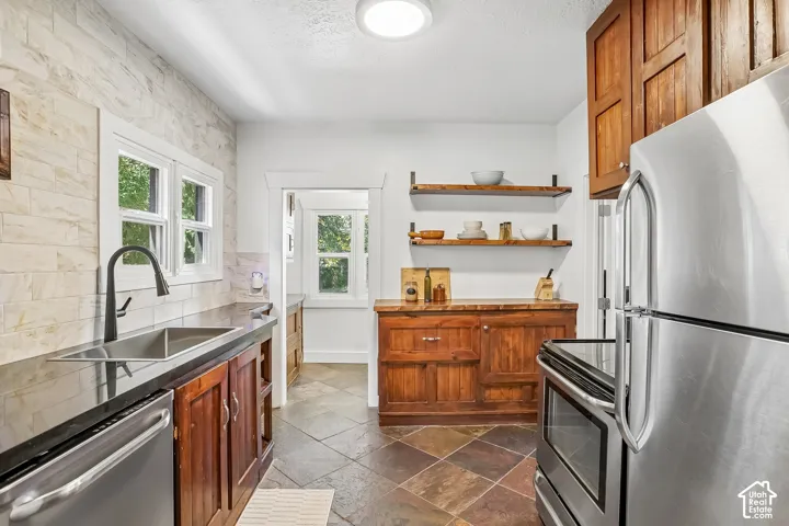 Kitchen featuring wood cabinetry, stainless steel appliances, dark countertops, and multi-tone tile flooring