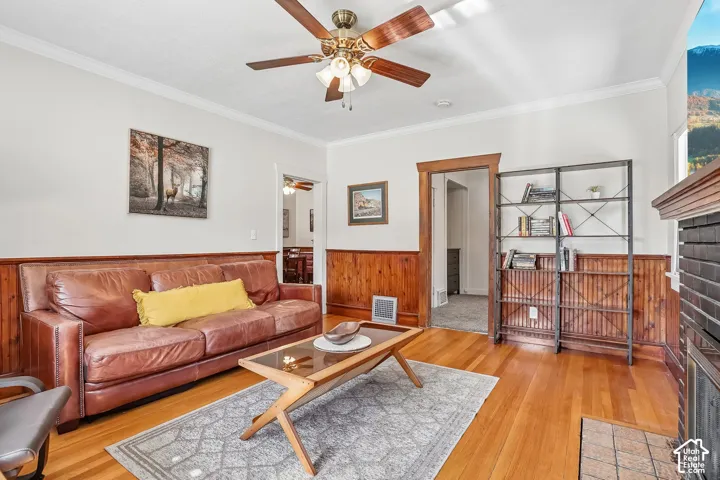 Wood-finish flooring, wood paneling, crown molding, and a ceiling fan with integrated lighting