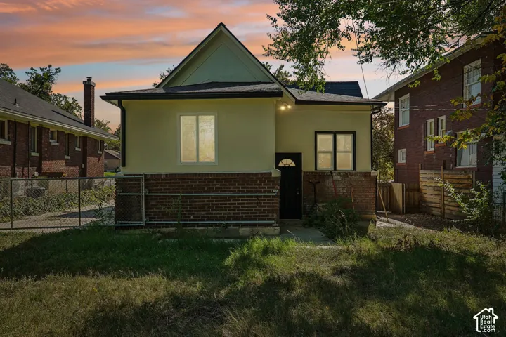 Exterior featuring a brick foundation, light-colored siding, dark-framed windows, and a dark entry door with an arched glass panel