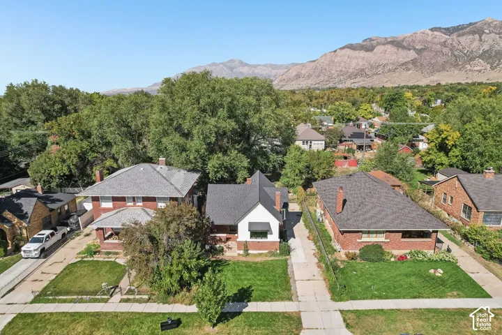 Red brick property with a gray shingle roof, chimney, and a landscaped front yard