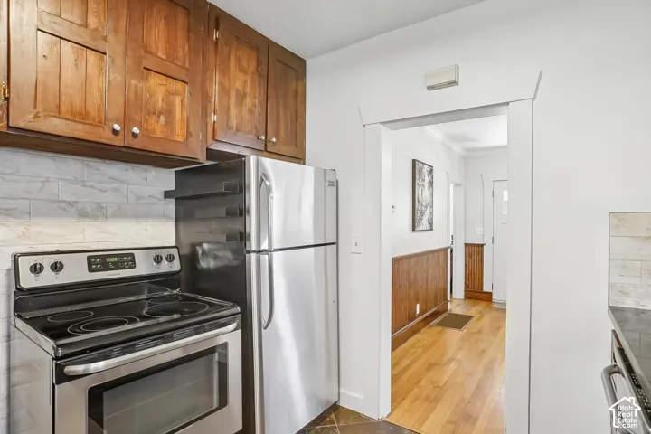 Wood cabinetry, stainless steel appliances, stone-look tile backsplash, wood-finish flooring, and wood wainscoting