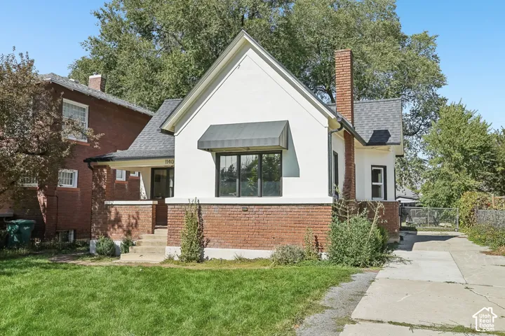 Exterior featuring white stucco and red brick siding, a dark roof, a brick chimney, and a front awning over a window