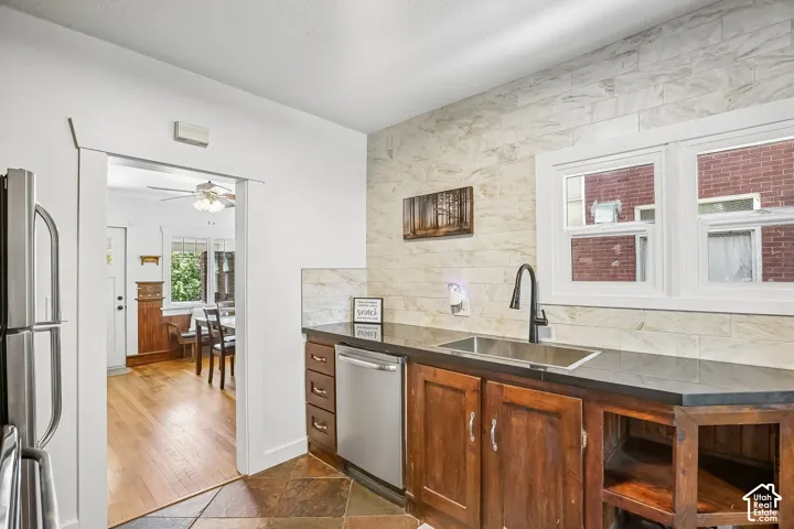 Kitchen featuring a stainless steel sink with a matte black faucet, dark wood-finish cabinetry, a stainless steel dishwasher, and a light-toned tile backsplash