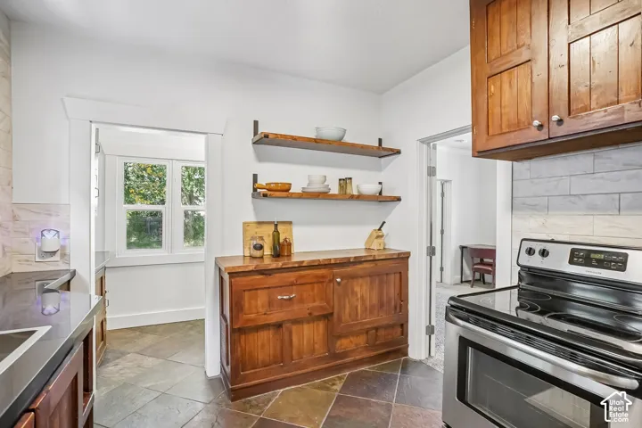 Slate tile flooring, open wood shelving, wood cabinetry, stainless steel range, and subway tile backsplash