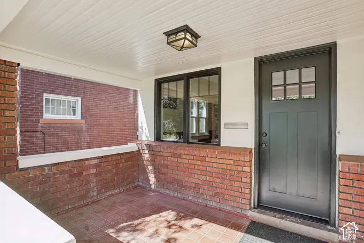 Covered front porch featuring brick siding, a paneled entry door with glass inserts, and a flush-mount ceiling light fixture