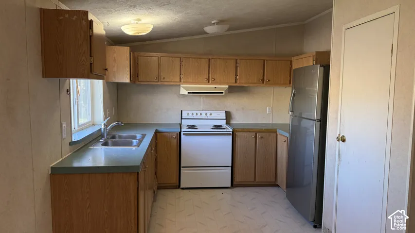Functional kitchen featuring a double basin stainless steel sink, light wood-finish cabinetry, and white appliances