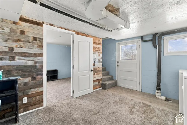 Carpeted flooring, wood-finish accent wall, and a door to backyard