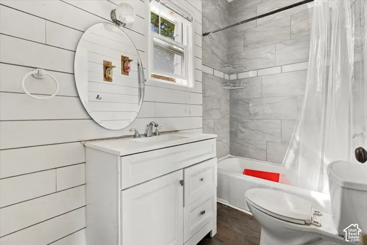 Bright bathroom featuring white subway tile walls, a circular framed mirror, white vanity with storage cabinetry, chrome fixtures, and wood-finish flooring