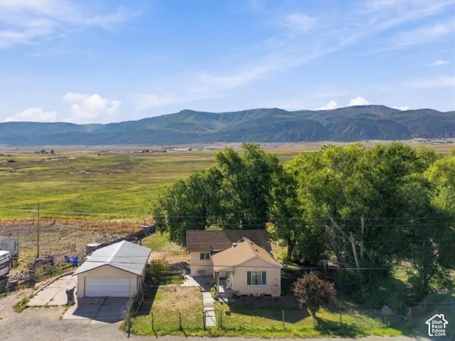 Scenic rural property featuring a single-story residence with attached garage, mature tree-lined landscaping, and expansive grounds overlooking mountain vistas and open valley terrain