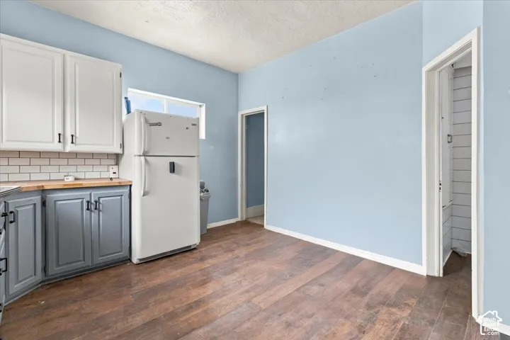 Wood-finish flooring, white upper cabinetry, gray lower cabinetry, wood-finish countertops, and subway tile backsplash
