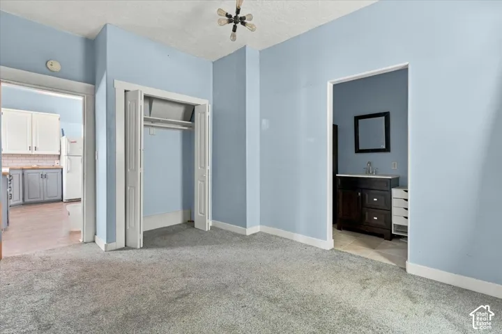 Carpeted room with a bi-fold closet, connected to a separate room featuring a dark wood-finish vanity with a white countertop and a wall-mounted mirror