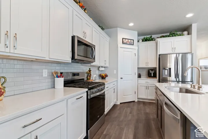 White shaker cabinetry, light-toned countertops, stainless steel appliances, grey subway tile backsplash, and wood-finish flooring