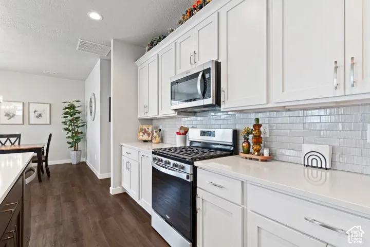 White shaker-style cabinetry, stainless steel microwave, stainless steel range, light-toned subway tile backsplash, and light-toned countertops